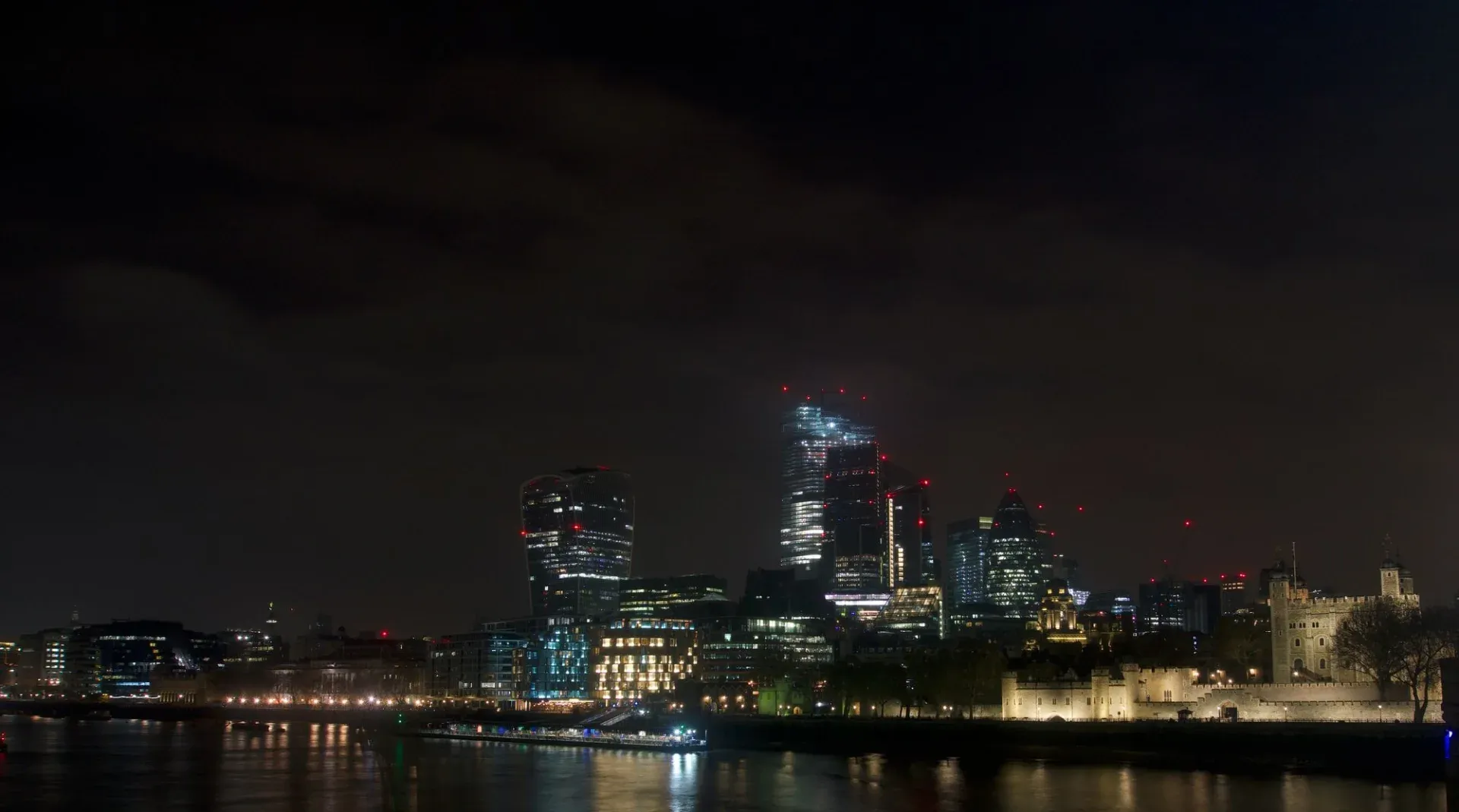 Vista nocturna espectacular del horizonte de Londres con rascacielos modernos y la histórica Torre de Londres.