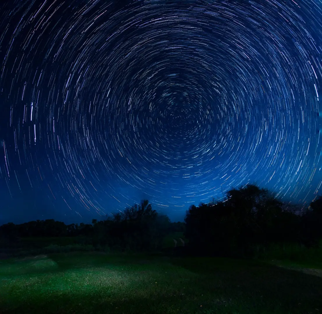 Vivid star trails creating a hypnotic pattern in a dark night sky over a tranquil outdoor landscape.