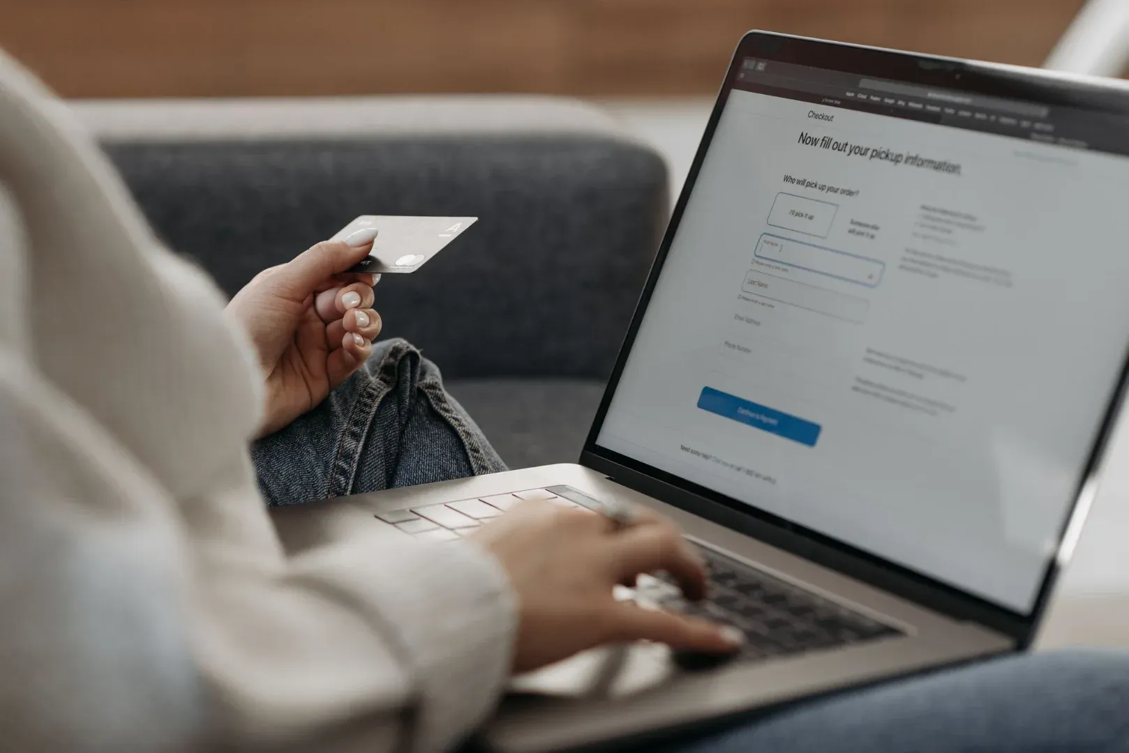 Woman holding credit card shopping online on a laptop from a couch.