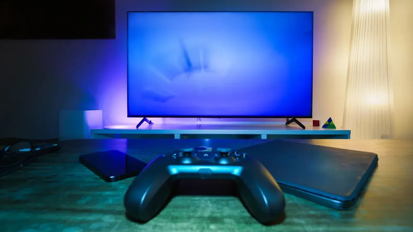 A stylish and ambient gaming setup featuring a controller, smart devices, and a TV in a lit living room.