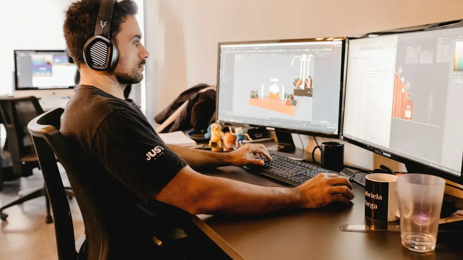 A man wearing headphones works on a computer with two monitors in a modern office setup.