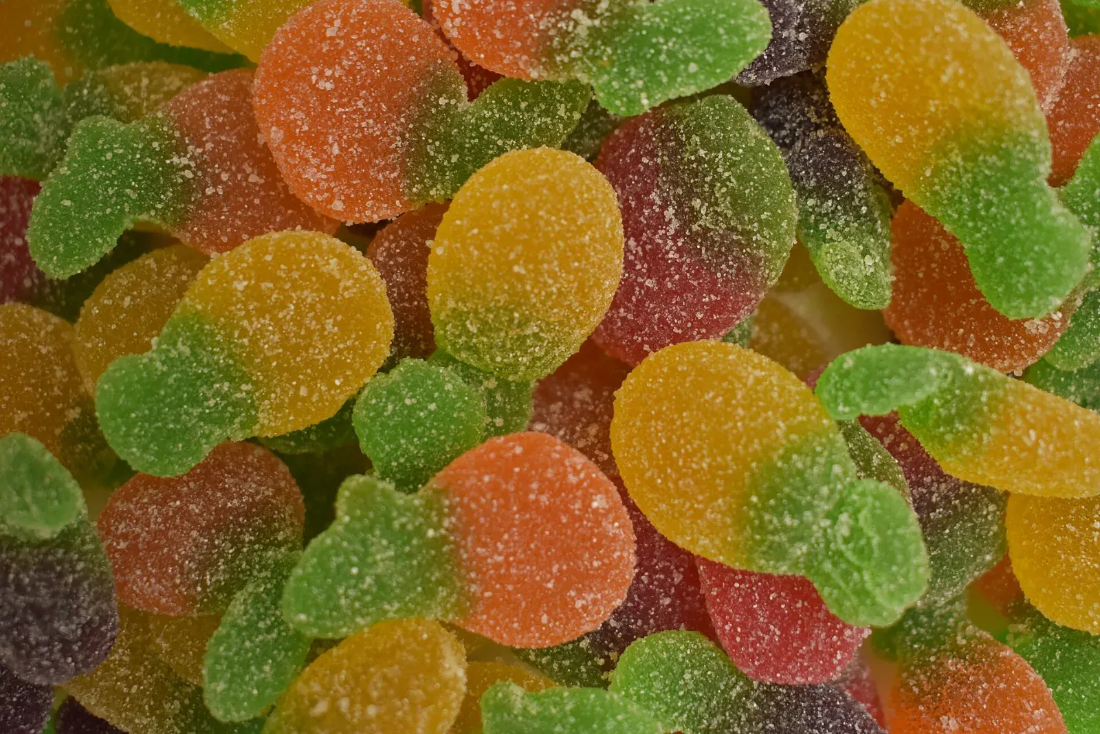 Primer plano de gomitas azucaradas con forma de fruta, en tonos naranja, amarillo, rojo y morado, con hojas de color verde.