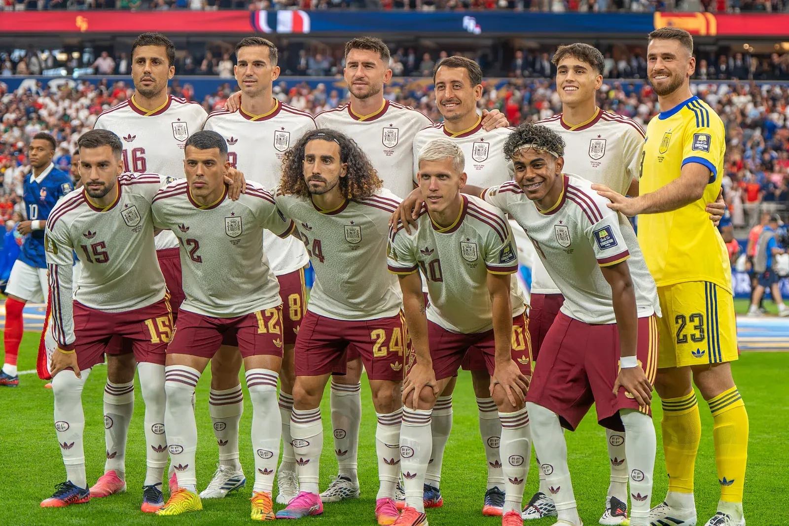 Los once titulares de España, con camiseta blanca y short granate, posan en dos filas sobre el césped; el portero viste de amarillo y la grada está llena al fondo.