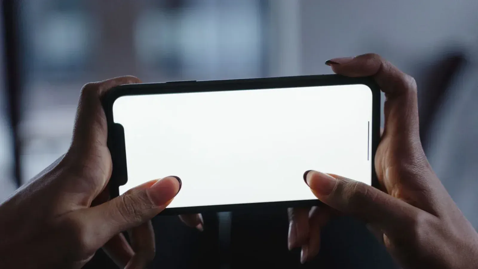 Vista cercana de manos sosteniendo un smartphone con una pantalla blanca en blanco, perfecta para diseños de maquetas.