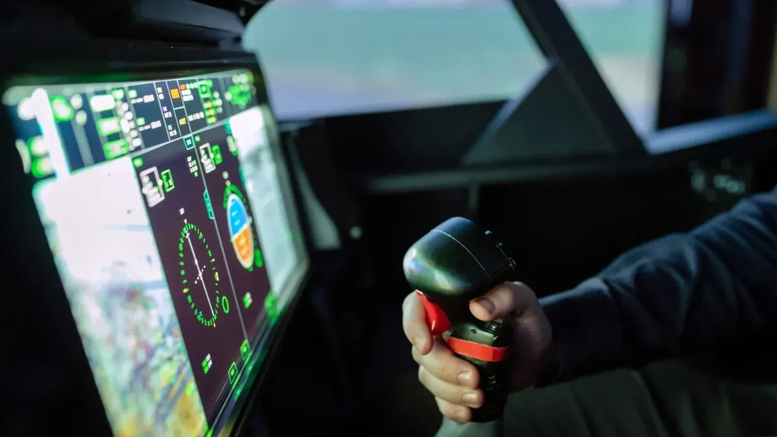 Primer plano de una cabina de avión simulada con joystick de control y pantalla digital.
