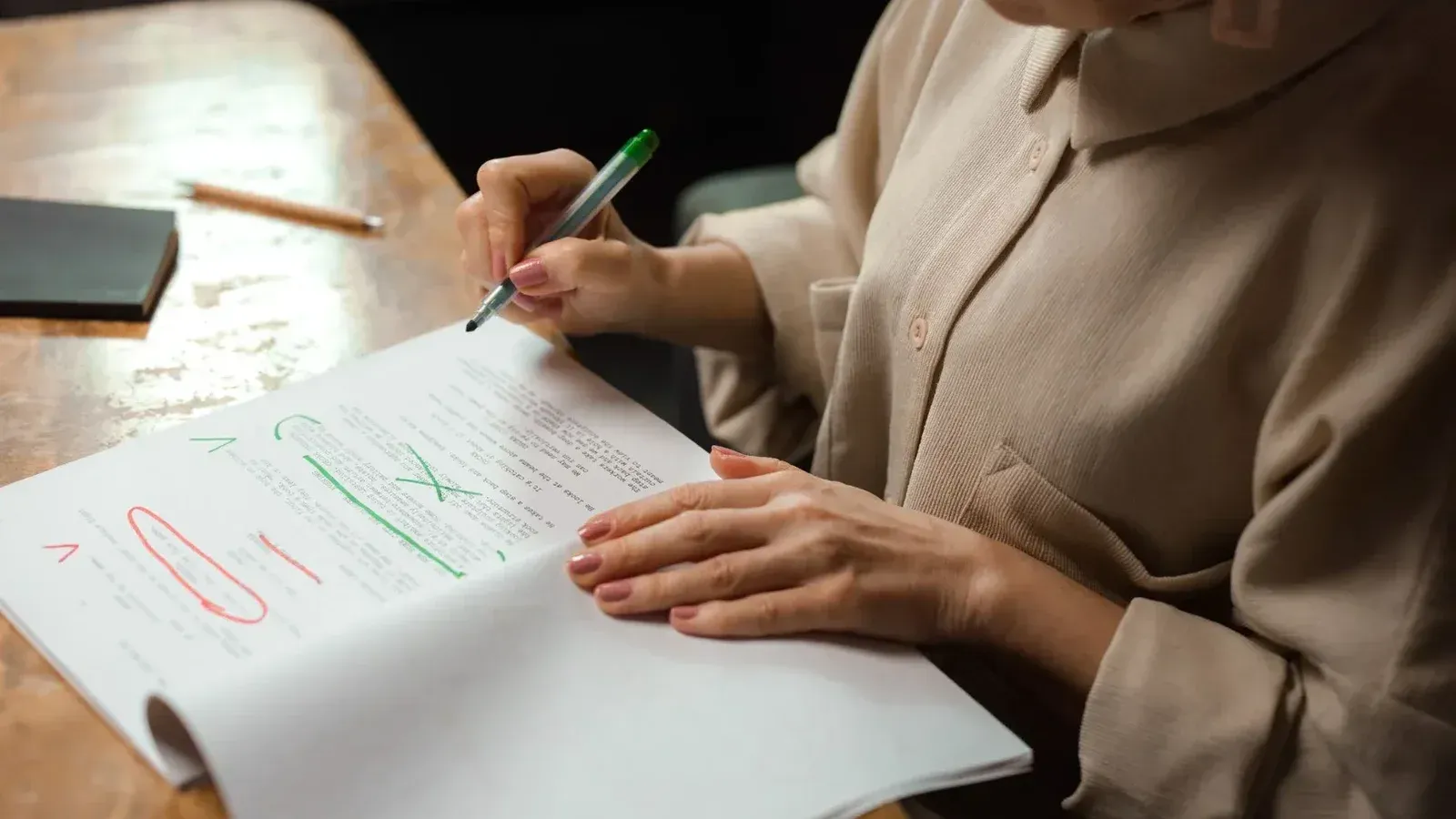 Close-up de una mujer mayor editando un manuscrito en un escritorio con un marcador verde en el interior.
