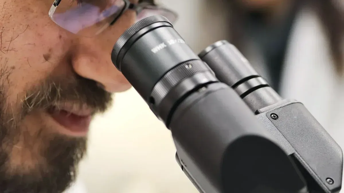 Primer plano de un científico examinando muestras usando un microscopio en un entorno de laboratorio.