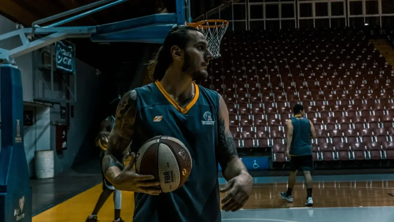 Male basketball players training and practicing in an indoor gym with basketballs and hoops.