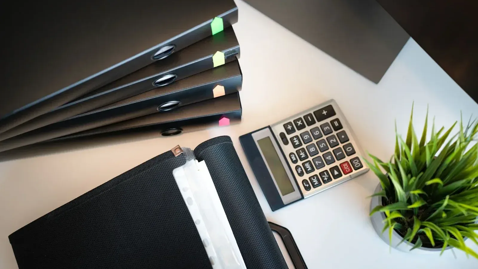 Vista superior de un escritorio de oficina ordenado con archivos, una calculadora y una planta, enfatizando la organización.