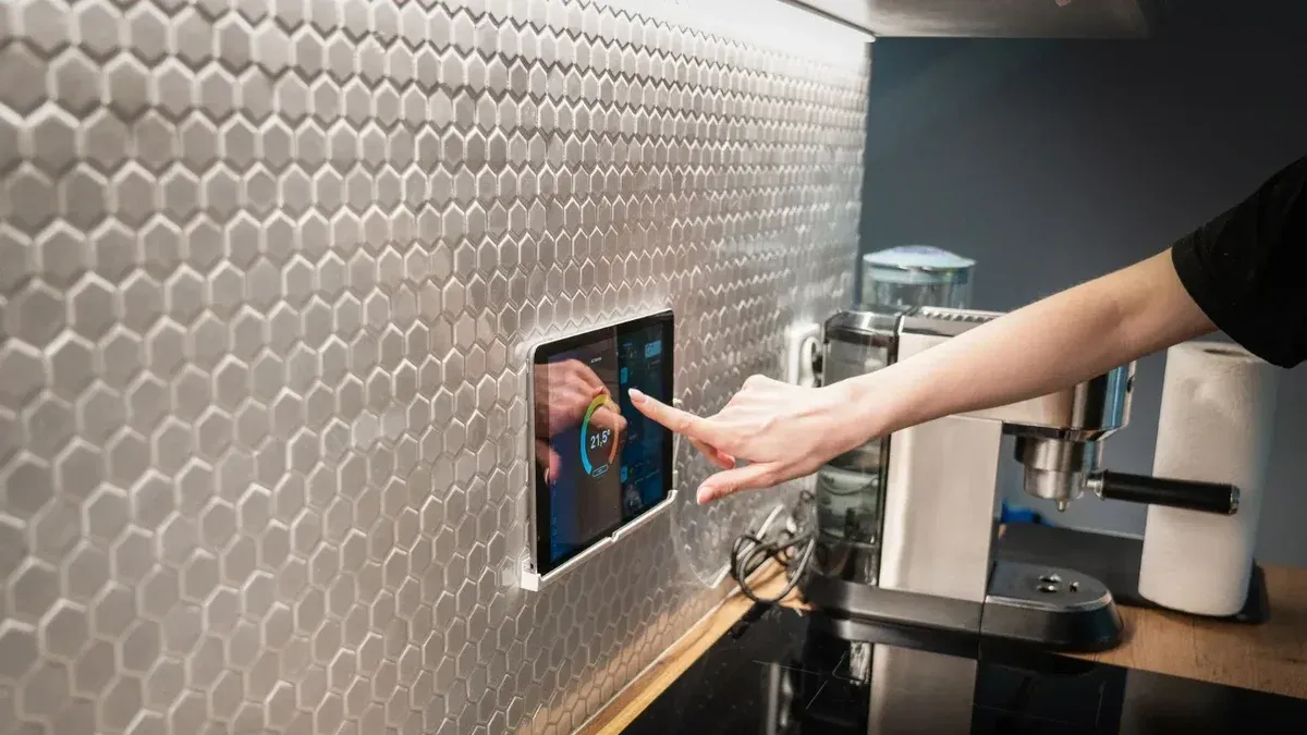A modern kitchen with a touchscreen smart home control panel integrated into a hexagon-patterned wall.