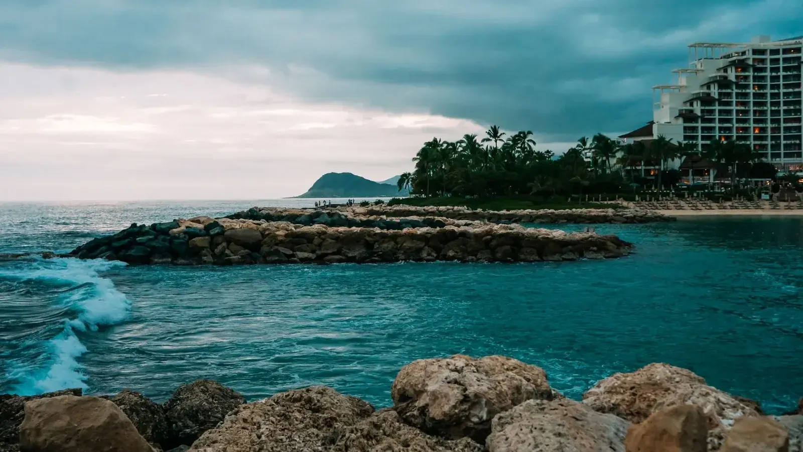 A stunning ocean view at Ko Olina, Hawaii with a resort and rocky shore under dramatic skies.
