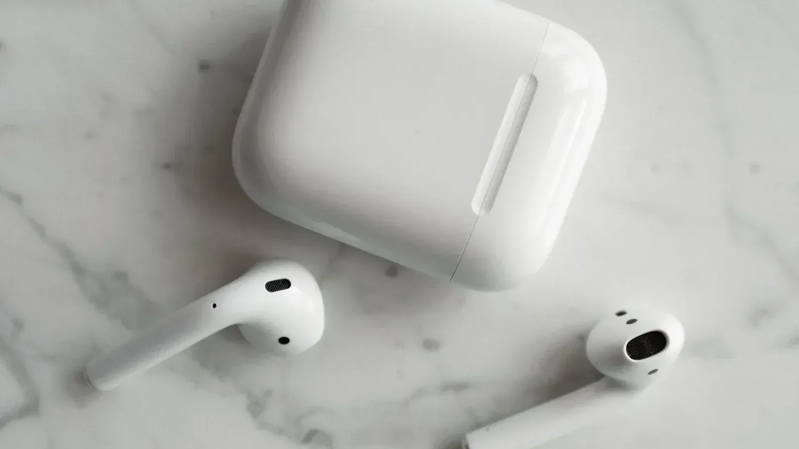 High-quality image of wireless earbuds and charging case on marble surface, showcasing modern technology.