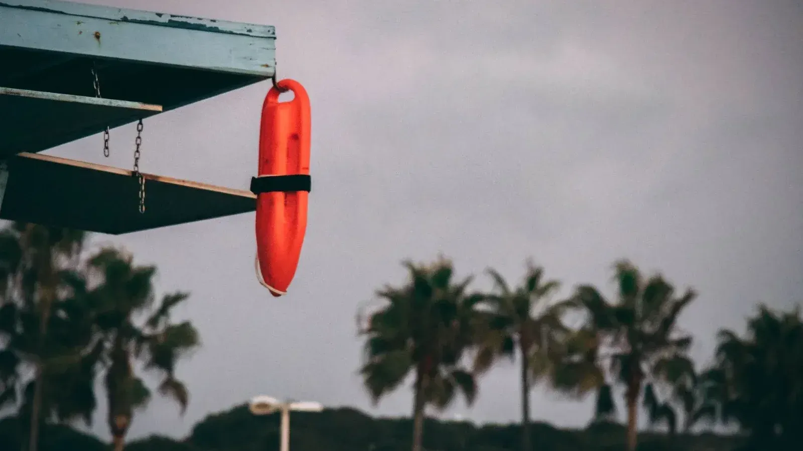 Orange lifeguard buoy hanging from a beach structure with palm trees in the background at sunset.