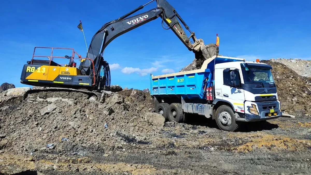 Excavadora cargando tierra en camión en un día soleado en un sitio de construcción.