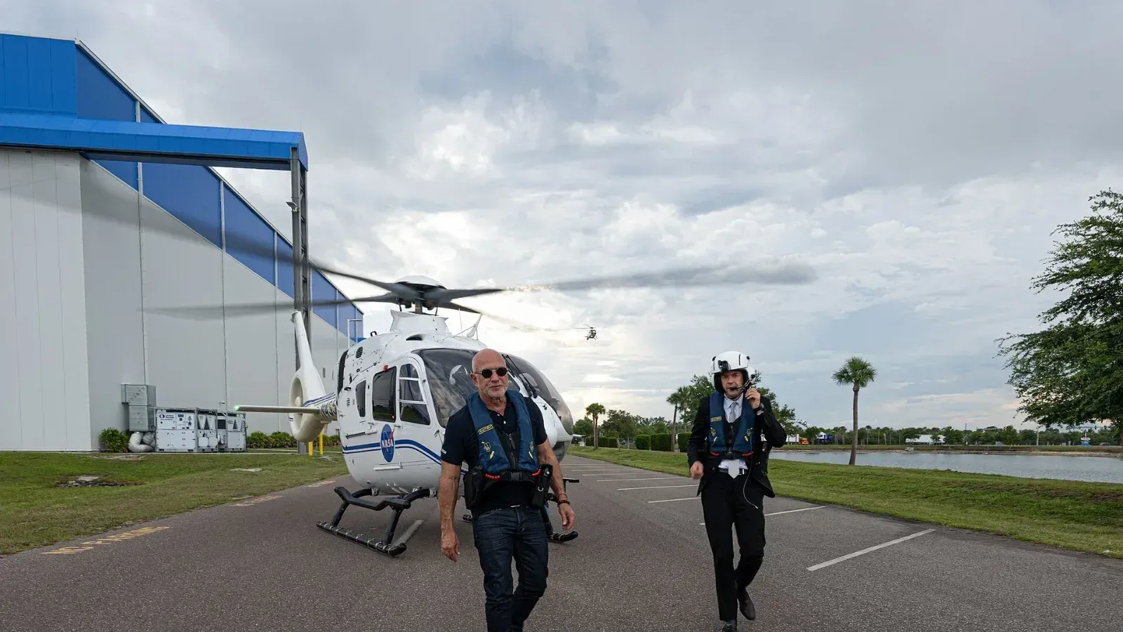 Jeff Bezos, con lentes oscuros y chaleco salvavidas, camina junto al administrador de la NASA, Jared Isaacman, frente a un helicóptero de la NASA en Blue Origin, Florida