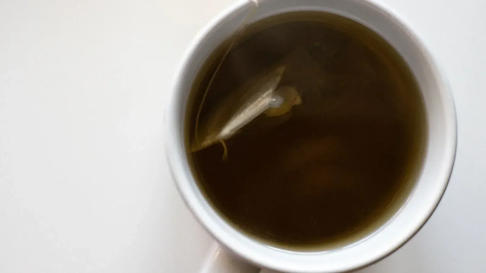 Top view of a white cup filled with fresh brewed green tea on a white background.