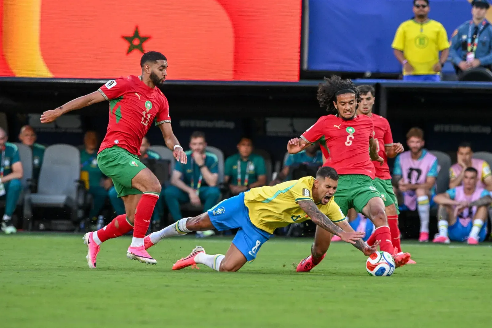 Bruno Guimarães, de Brasil, cae al césped mientras disputa el balón con Ismael Saibari y Ayyoub Bouaddi, de Marruecos, junto al banquillo