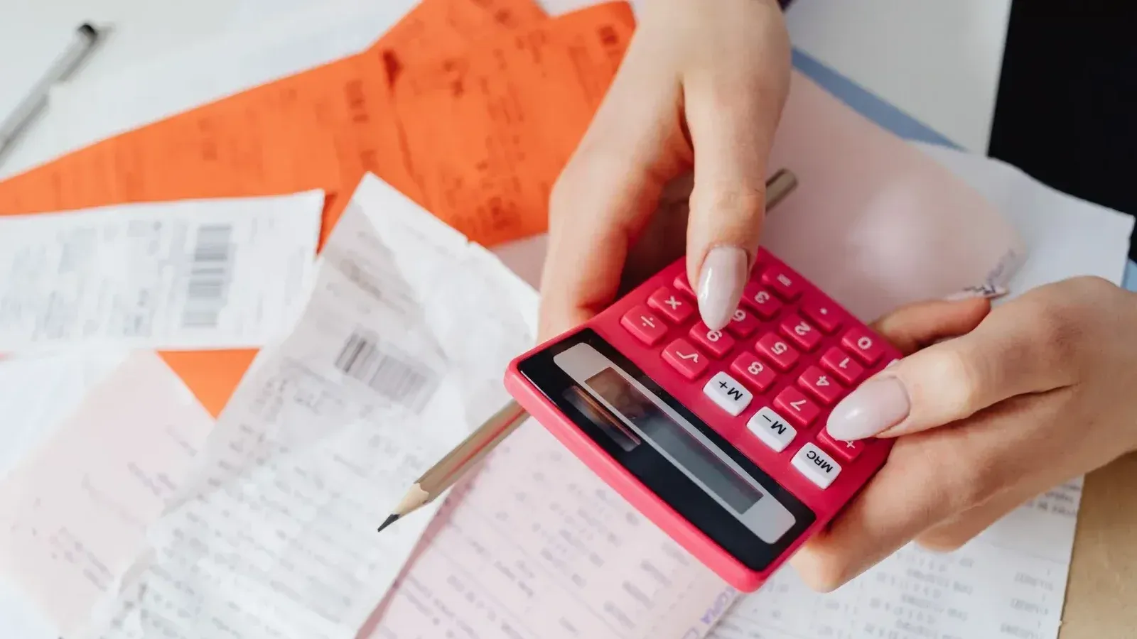 Manos usando una calculadora rosa para administrar los gastos en medio de varios recibos y documentos.