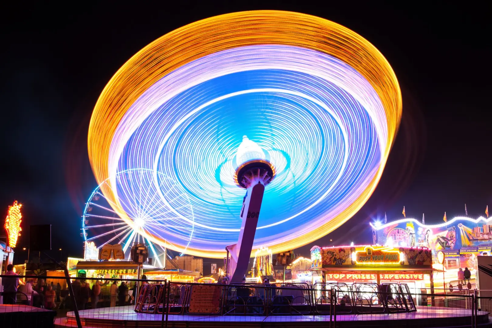 Captura de larga exposición de un colorido paseo en un parque de diversiones por la noche, mostrando luces giratorias.