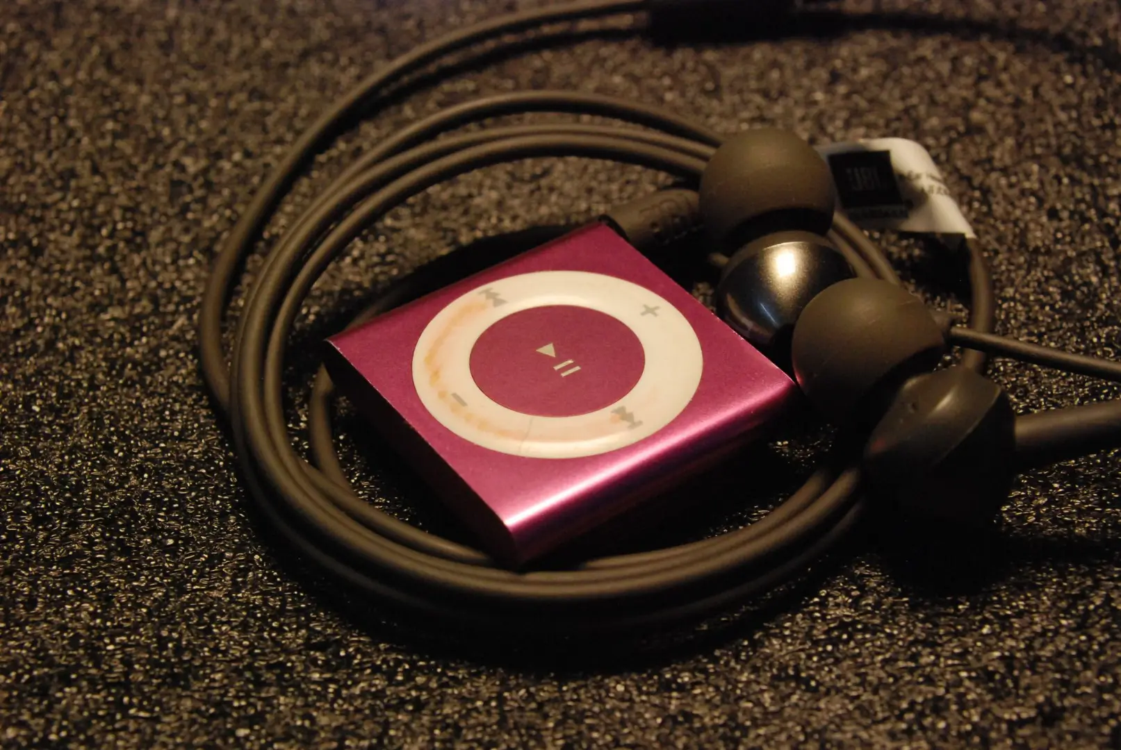 Close-up of a pink MP3 player with earphones coiled around it on a textured surface.