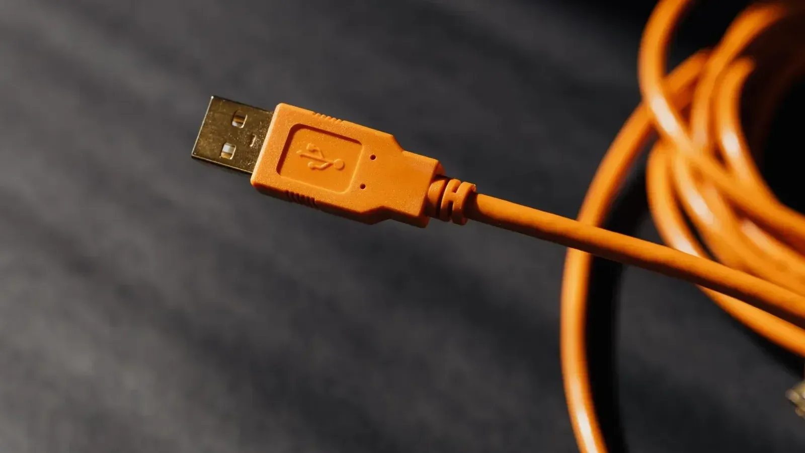 Foto macro detallada de un conector de cable USB naranja con enfoque en la textura.