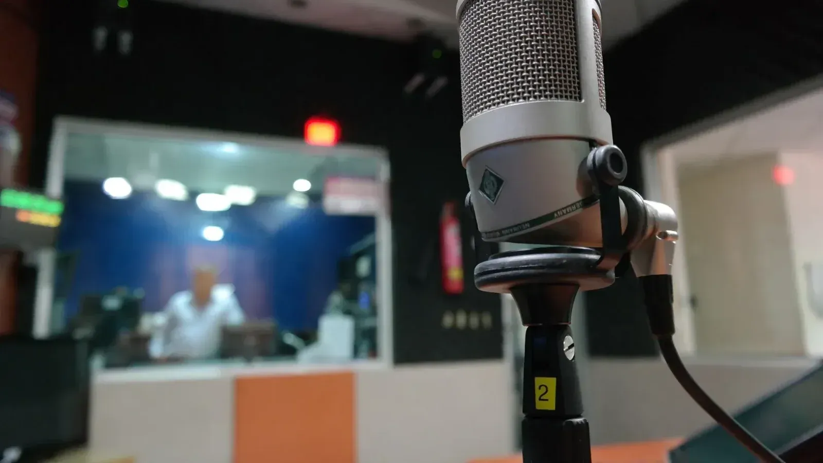 Primer plano de un micrófono en un estudio de grabación con un ingeniero de sonido borroso en el fondo.