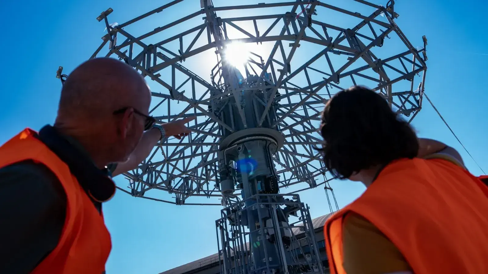 Deux membres des équipes techniques, vêtus de gilets de sécurité orange, observent la structure métallique de la future attraction Wilderness Explorers Sky Swings à Disney Adventure World.