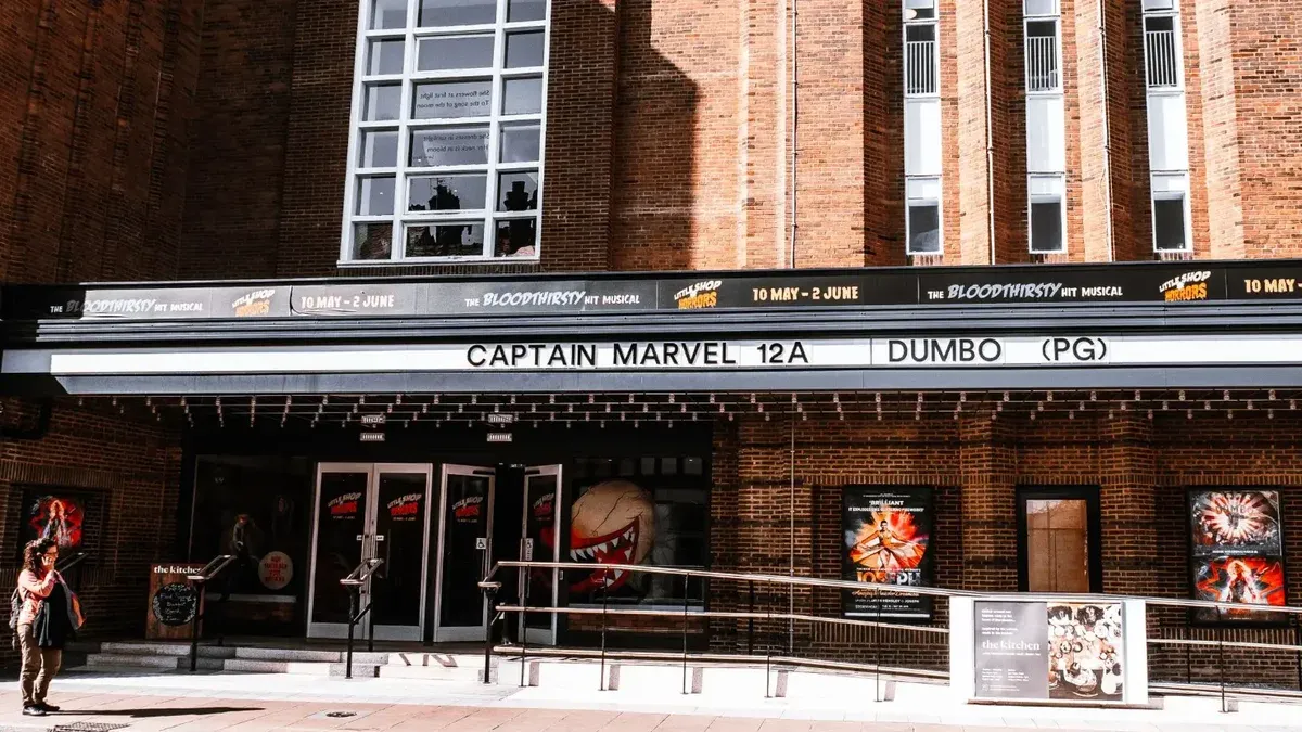 Exterior view of a brick theater showcasing current movie advertisements in an urban setting.