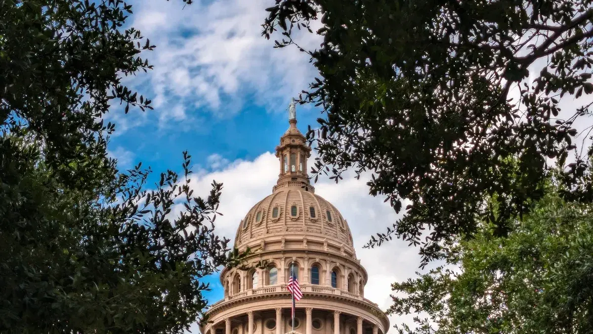 View of the iconic Texas State Capitol dome framed by lush trees under a vibrant sky in Austin, TX.