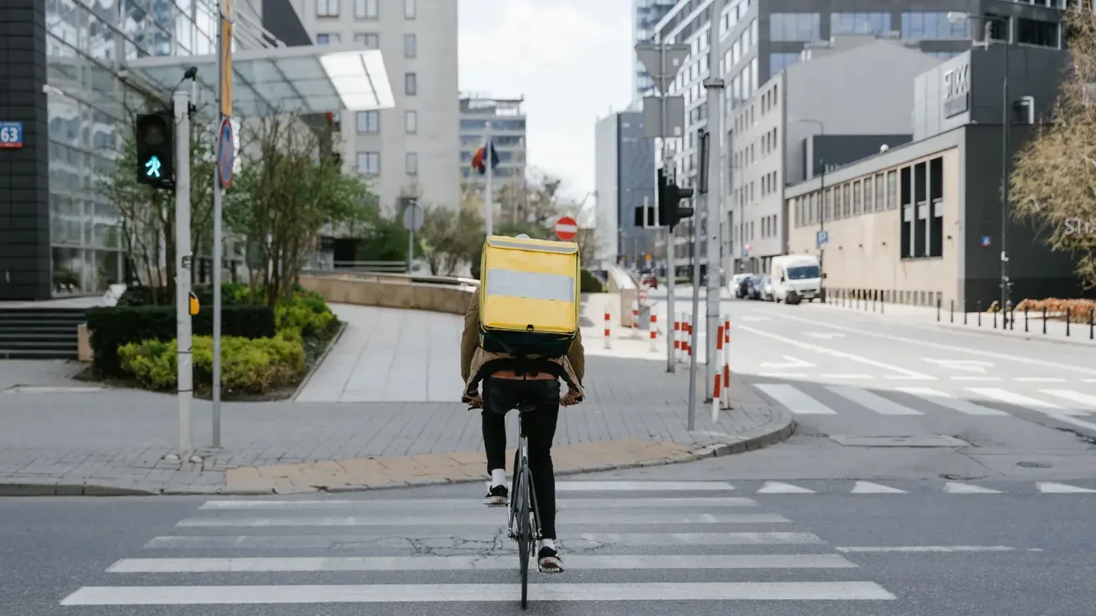 Ciclista con bolsa térmica cruzando la calle en el centro de Varsovia, Polonia.