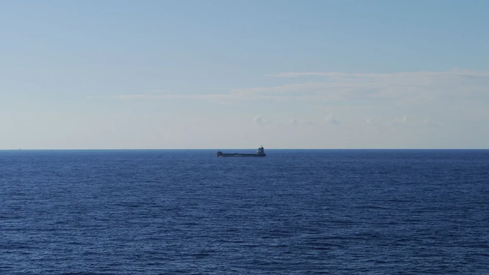 Una escena tranquila de un barco de graneles que cruza un vasto océano abierto bajo un cielo azul despejado.