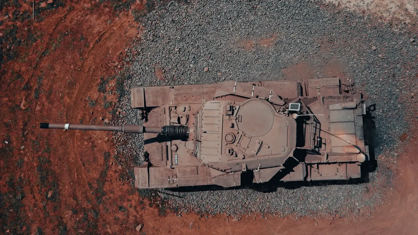 Aerial shot of a military tank parked on rugged terrain captured by drone.