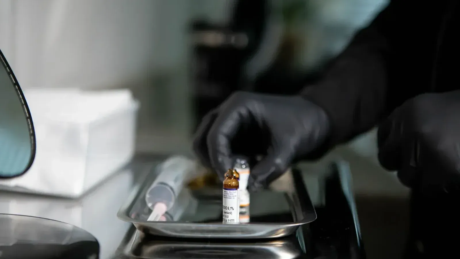 Close-up of gloved hands arranging medicine vials on a tray in a clinical setting.