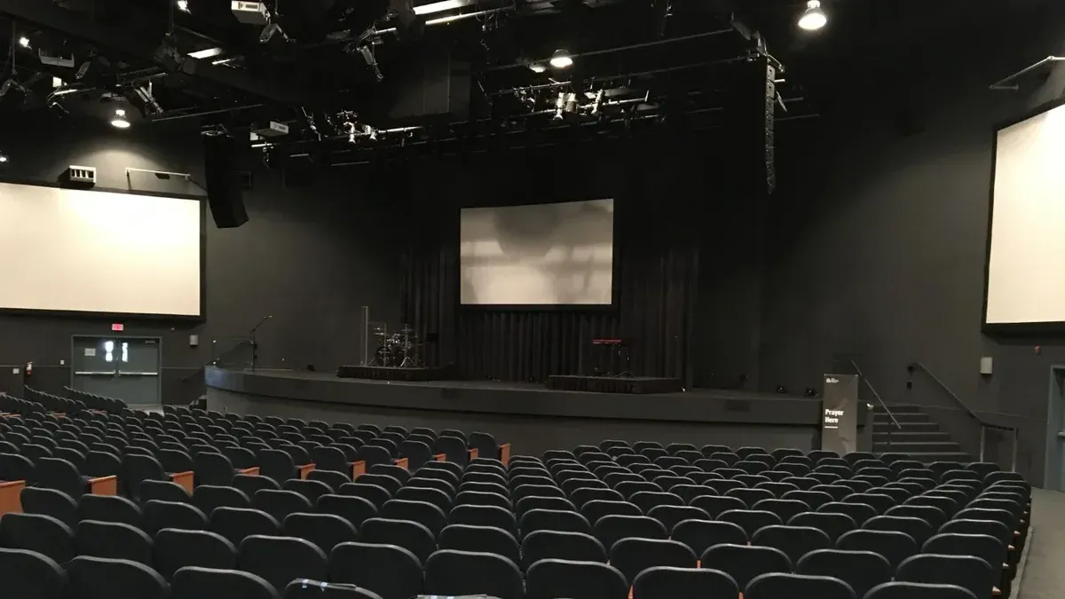 Rows of comfortable empty seats in modern theater hall with stage and screens