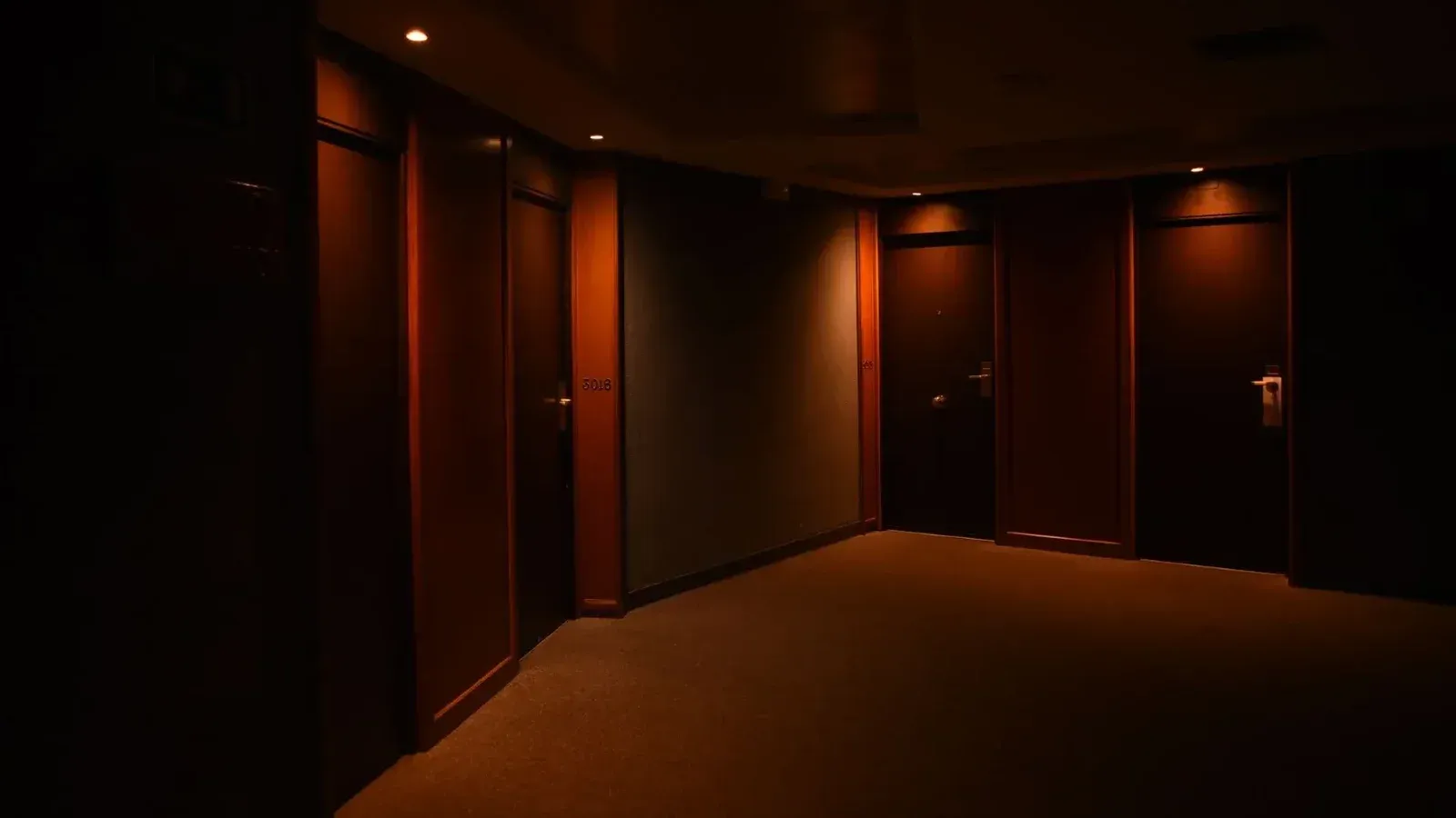 Un pasillo de hotel oscuro y silencioso con múltiples puertas de madera cerradas e iluminación suave.