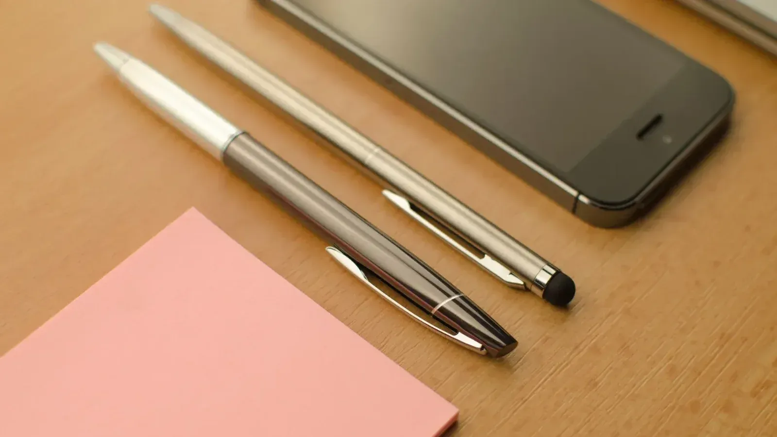 Stylish workspace featuring a smartphone, pens, and a notepad on a wooden desk.