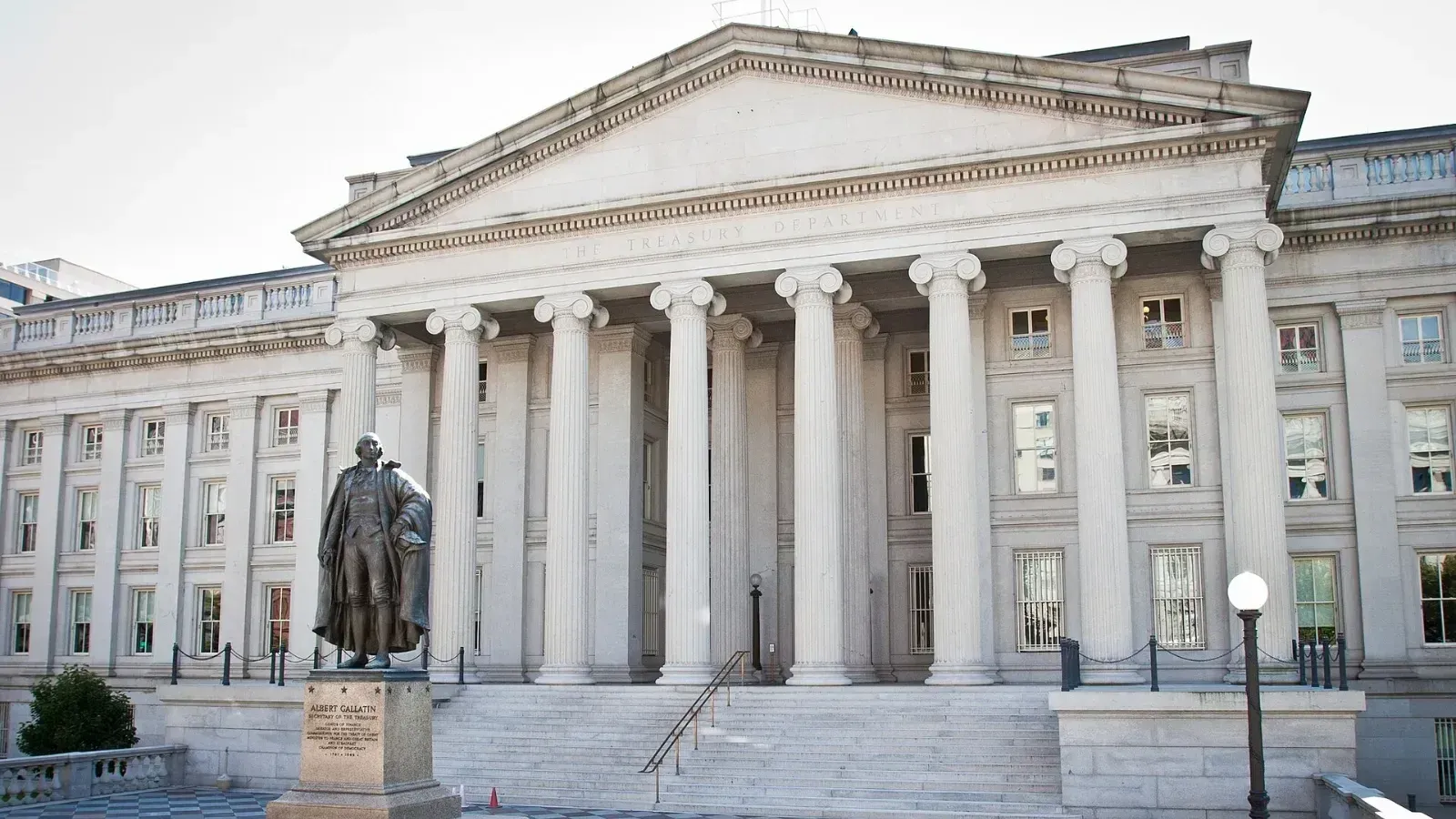 Fachada del edificio del Departamento del Tesoro de Estados Unidos en Washington, con columnas, escalinata y una estatua de bronce al frente.