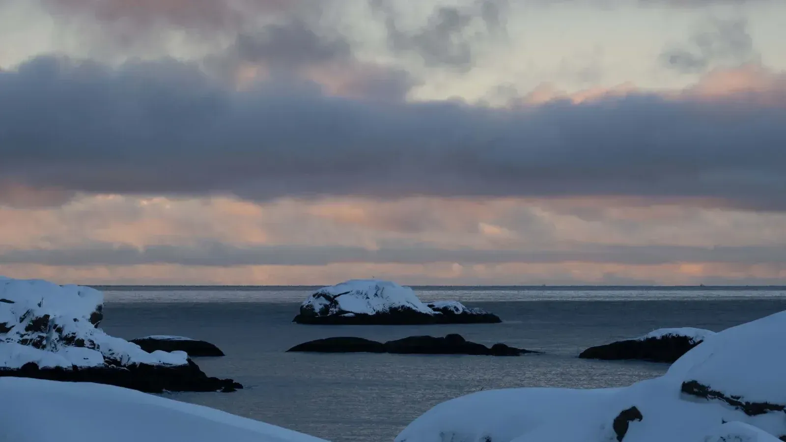 Serene winter coastal scene with snow-covered rocks and twilight sky.