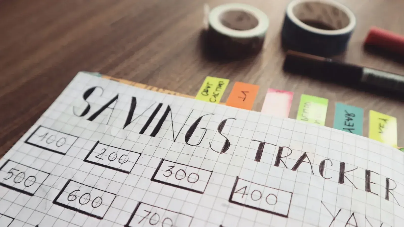 Primer plano de un rastreador de ahorros hecho a mano con pestañas de colores sobre una mesa de madera, ideal para la planificación financiera.