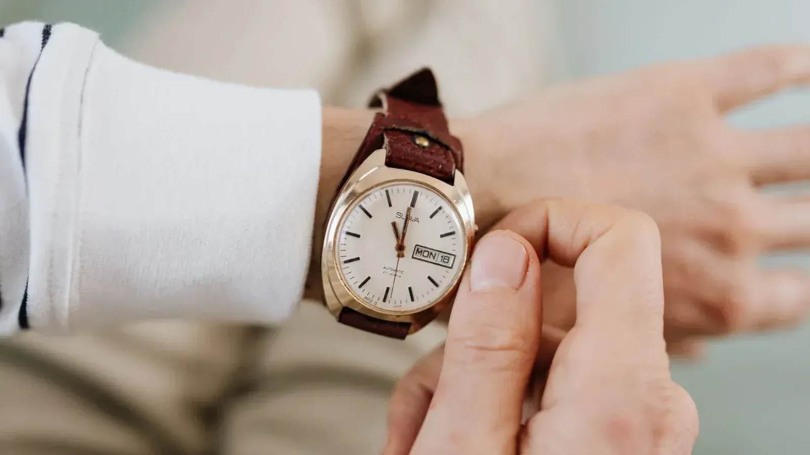 Un primer plano de una persona que ajusta un reloj de pulsera analógico con correa de cuero marrón vintage.