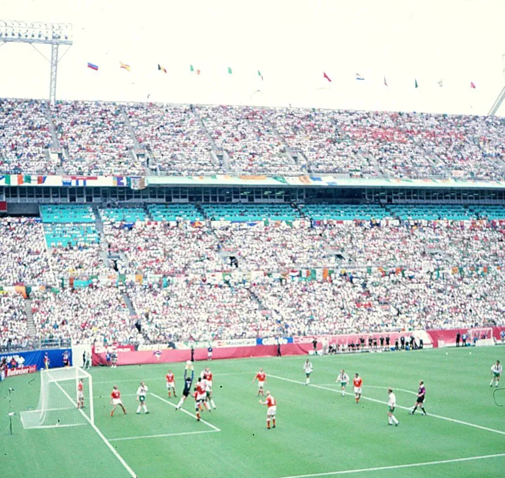 Estadio con las gradas llenas; en el área, un portero salta y atrapa el balón entre jugadores de camiseta anaranjada y otros de camiseta blanca y pantalón verde.