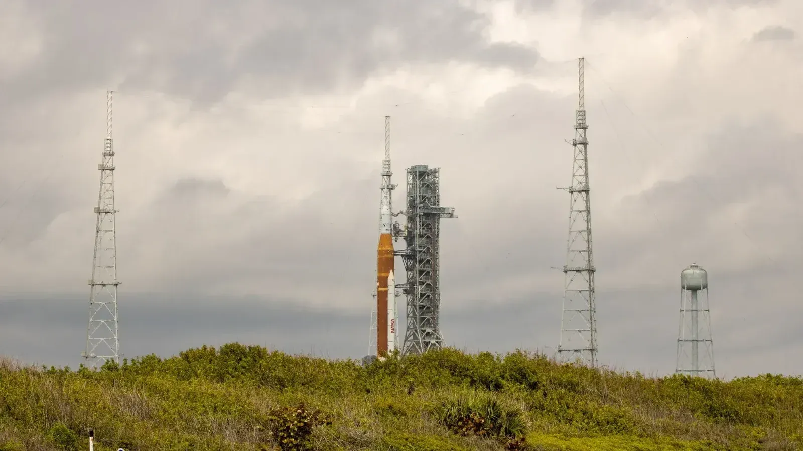 Cohete de la NASA en la plataforma de lanzamiento rodeado de antenas contra un cielo nublado.