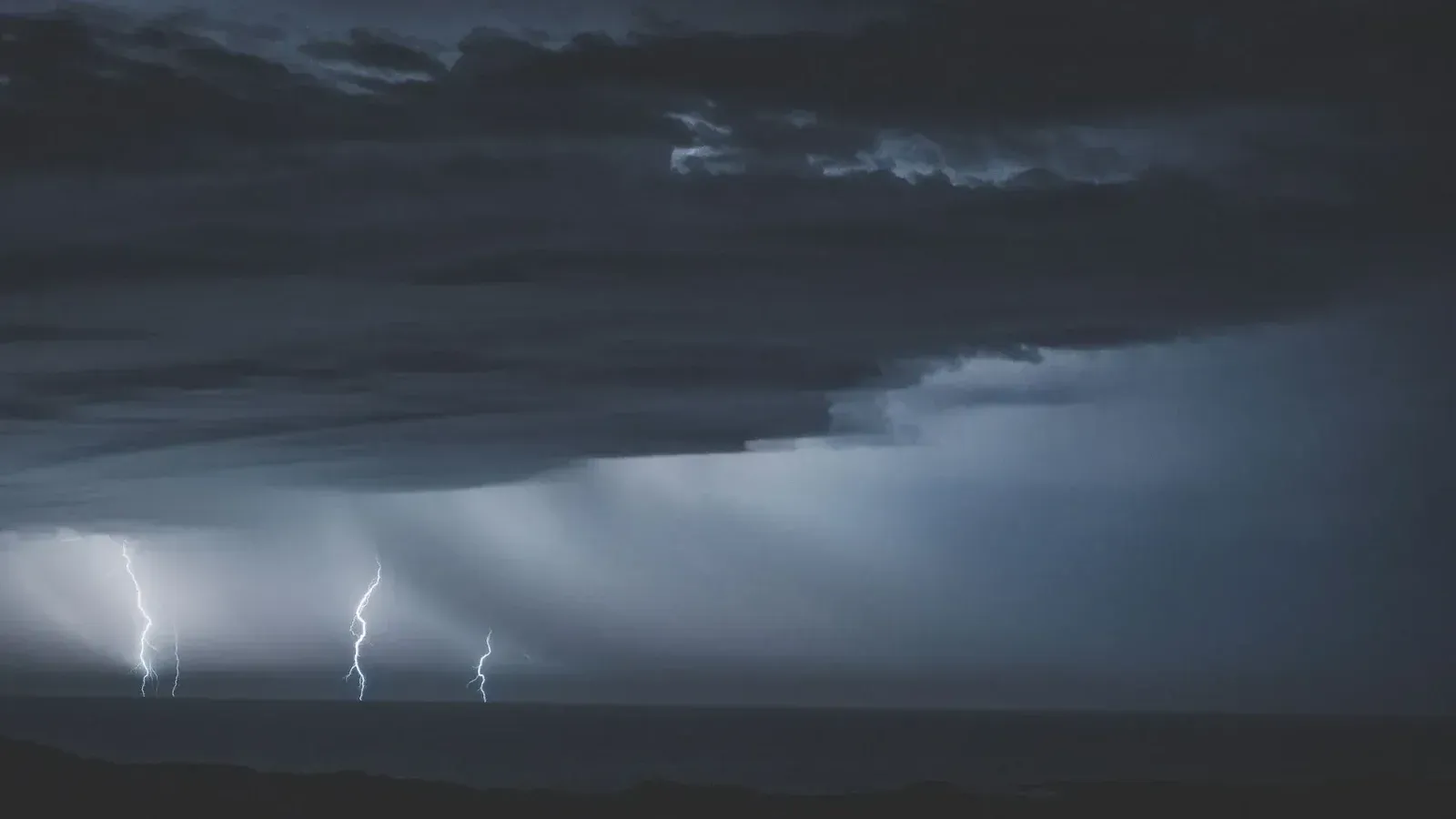 Peligrosos relámpagos brillantes en el cielo nublado y sombrío sobre el agua interminable del océano en la noche