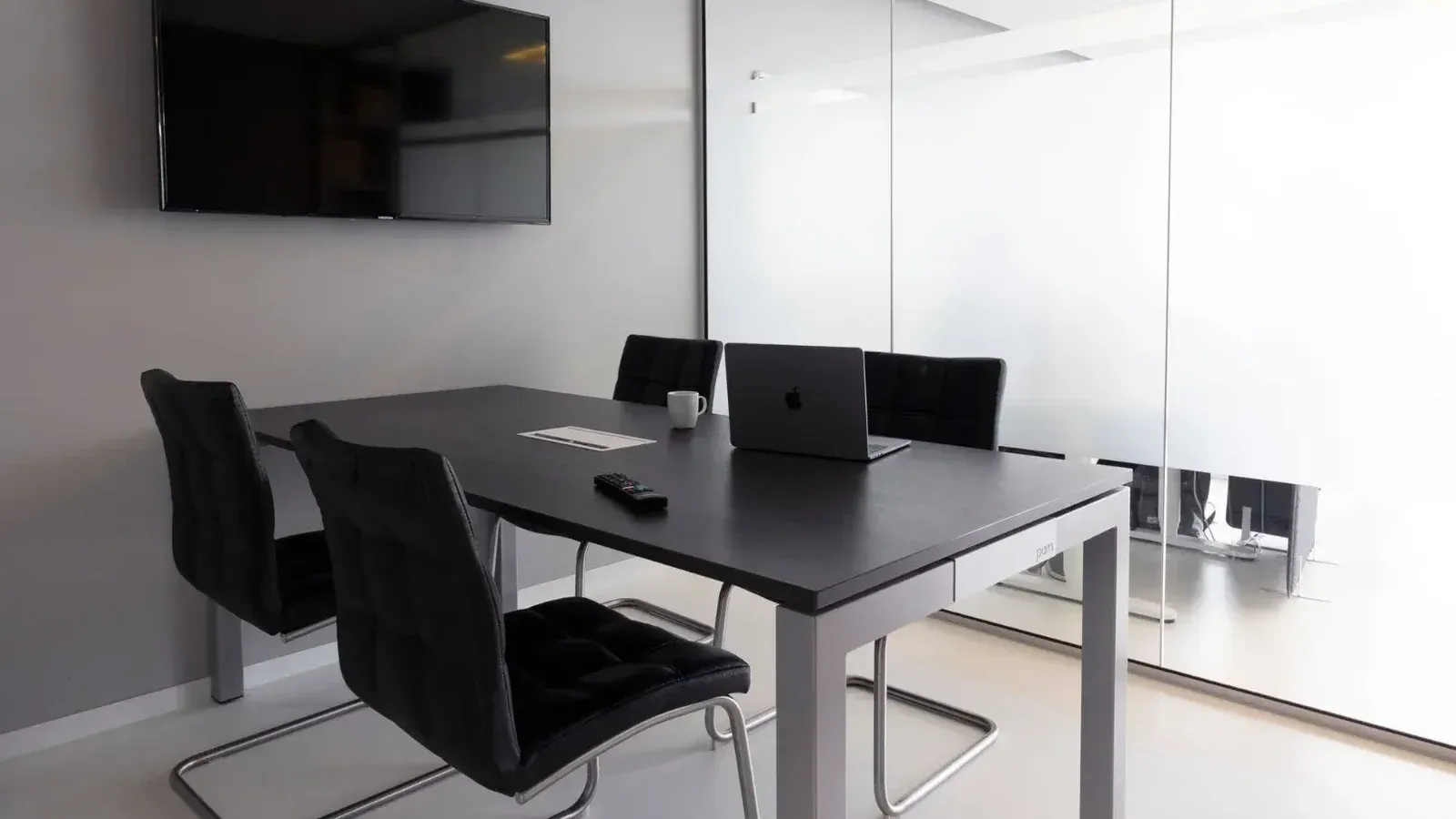 Sala de reuniones contemporánea con paredes de vidrio, computadora portátil y televisión para discusiones de negocios.