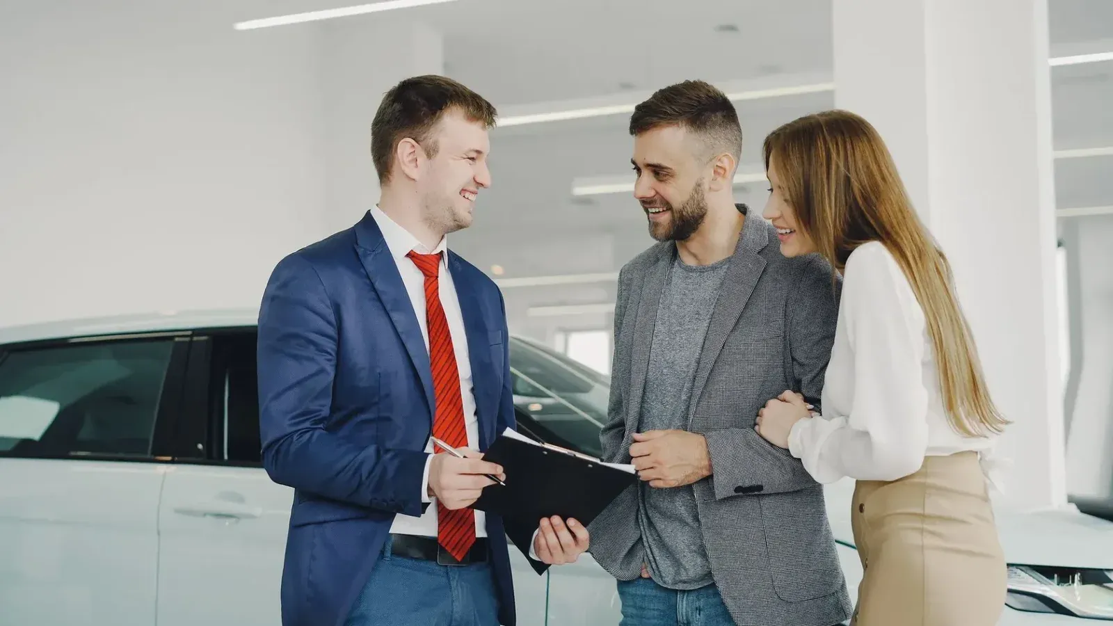 Una pareja sonriente compra un automóvil nuevo a un vendedor seguro dentro de un concesionario de automóviles moderno.