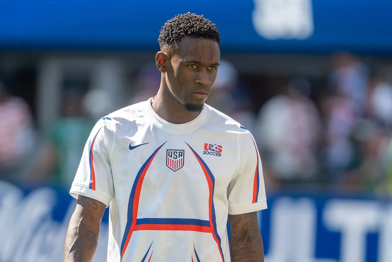 Folarin Balogun, con la camiseta blanca de Estados Unidos, mira al frente con la grada desenfocada al fondo.