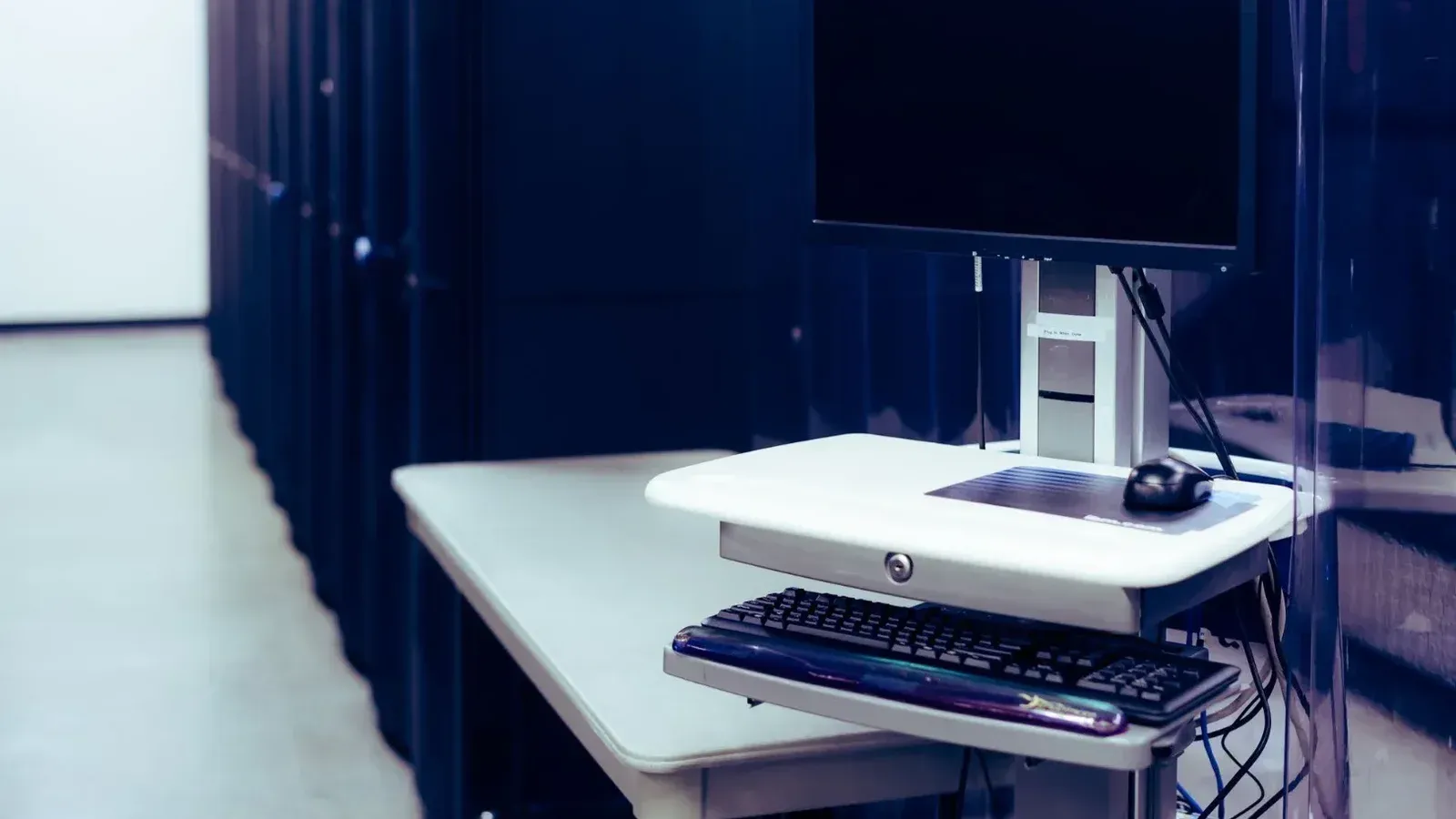 Computadora contemporánea con pantalla negra colocada en stand cerca de la fila de bastidores de acero del servidor en el centro de datos