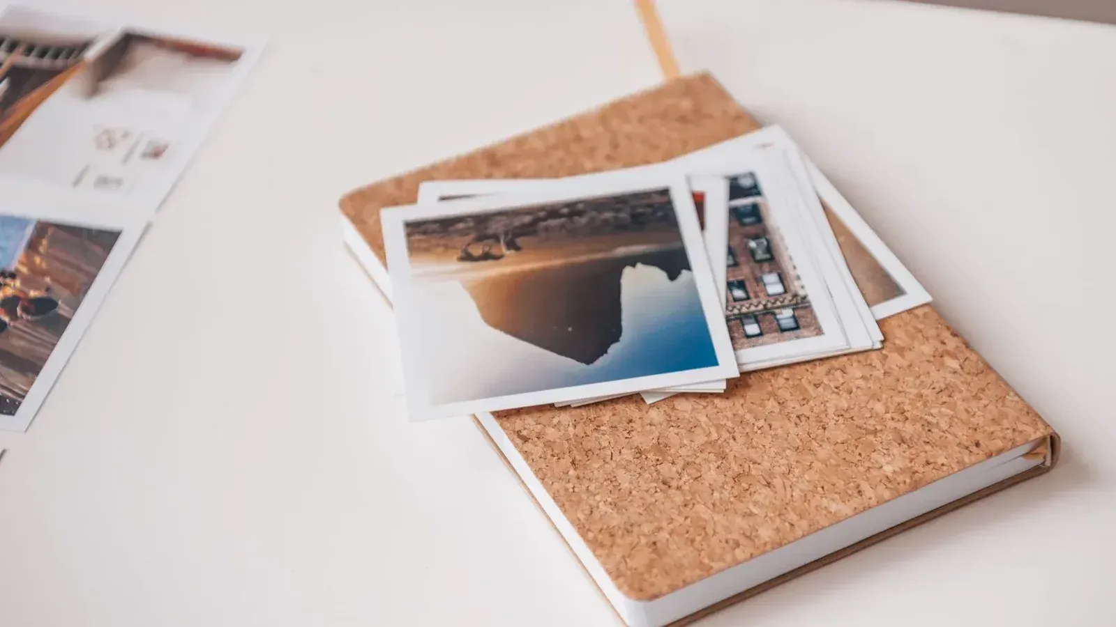 Cuaderno cubierto de corcho con fotografías impresas en un escritorio blanco, transmitiendo recuerdos de viaje.