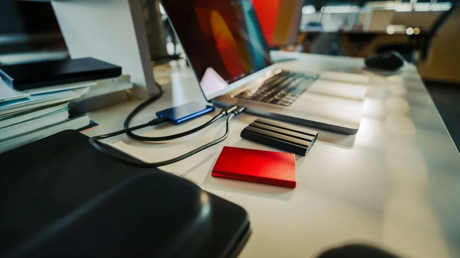 Un escritorio de oficina cuidadosamente organizado con una computadora portátil y varios discos duros externos, perfecto para un espacio de trabajo digital.