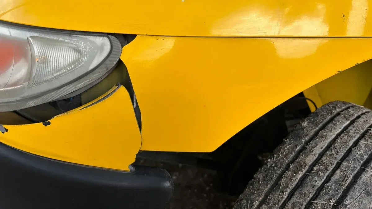 Close-up image of a yellow car's damaged front bumper and headlight for insurance or accident concept.